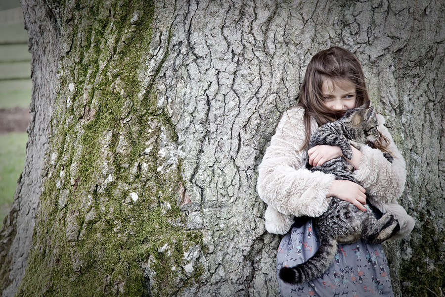 Girl holding a cat leaning against a tree