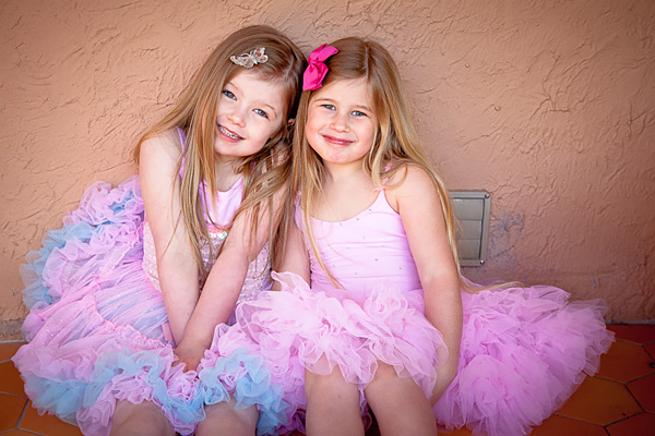 Two small girls in pink dresses sitting on a bench